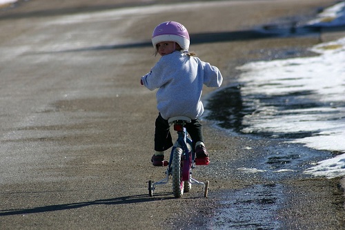 girl using training wheels to ride bike